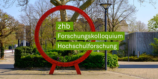 zhb Forschungkolloquium Hochschulforschung Foto des roten Zahnrads auf dem Martin-Schmeißer-Platz an der TU Dortmund. Aus dem Zahnrad ragt von links nach rechts der Schriftzug zhb Forschungskolloquium Hochschulforschung heraus