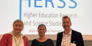 Prof. Leisyte, Prof. Flatten und Prof. Wilkesmann am Rednerpult, im Hintergrund das Logo der Tagung