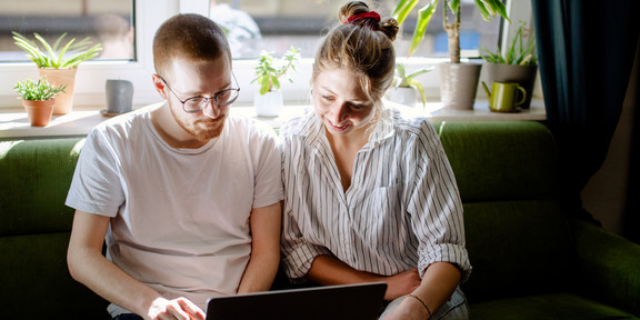 Two students working on a laptop, sitting on a sofa.