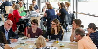 Teilnehmende eines Workshops sitzen an einem runden Tisch und diskutieren.